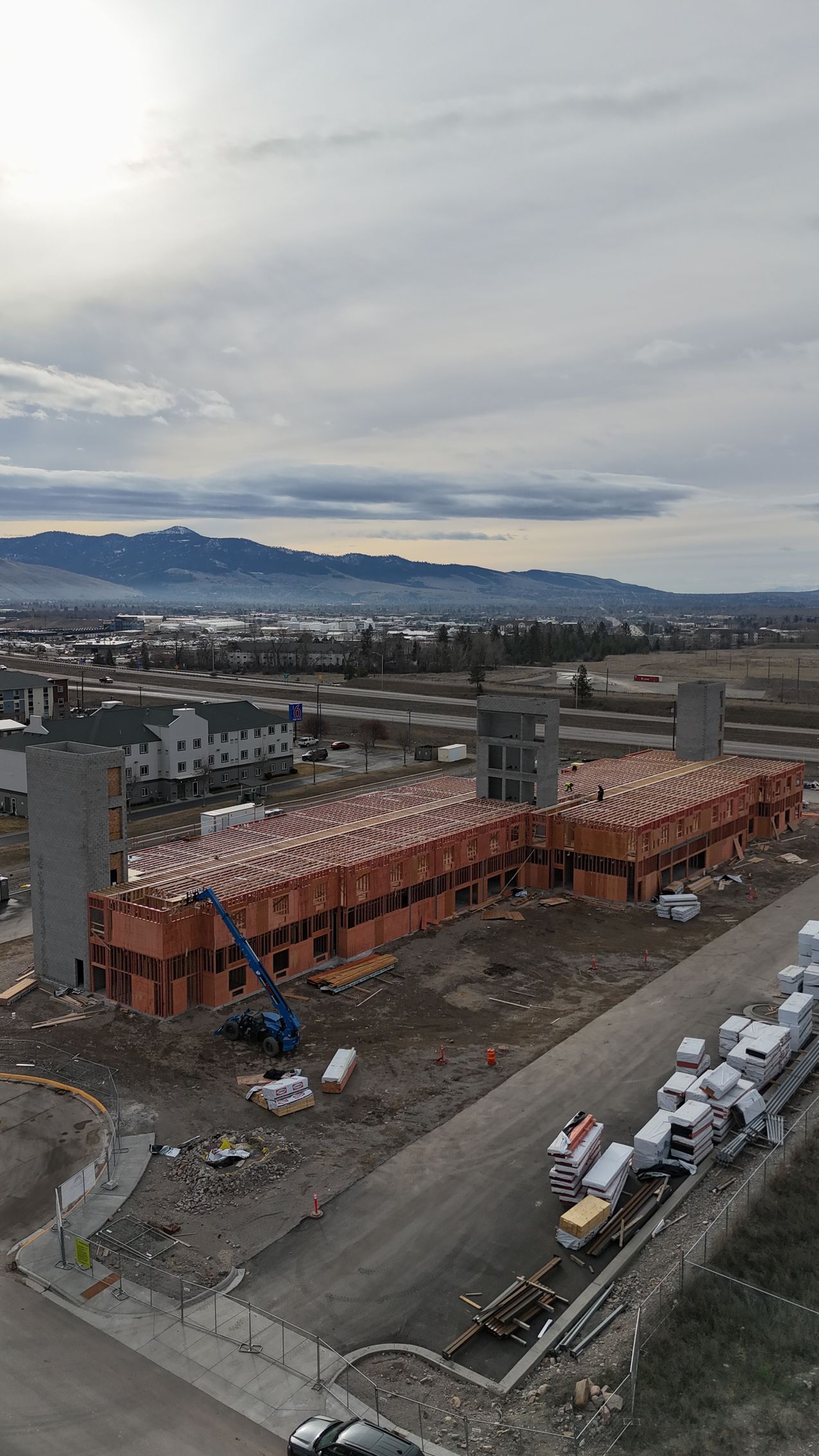Construction site with a long red-brick building frame and mountains under a cloudy sky in the distance