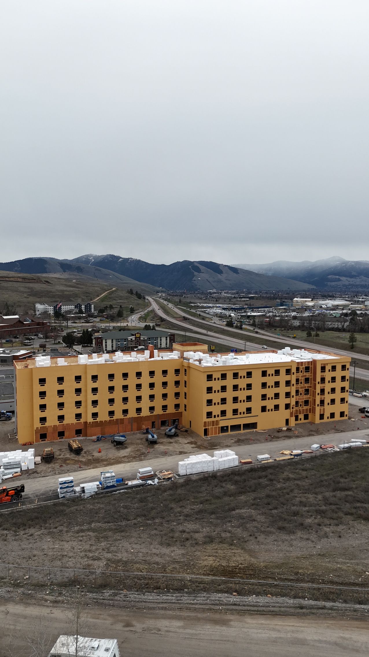 Yellow apartment building under construction in a snowy landscape with overcast sky and distant hills