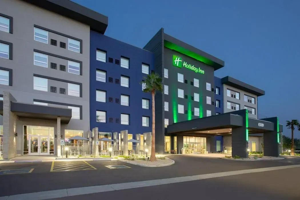 Modern hotel exterior at dusk with illuminated entrance, blue and gray facade, and green-lit sign