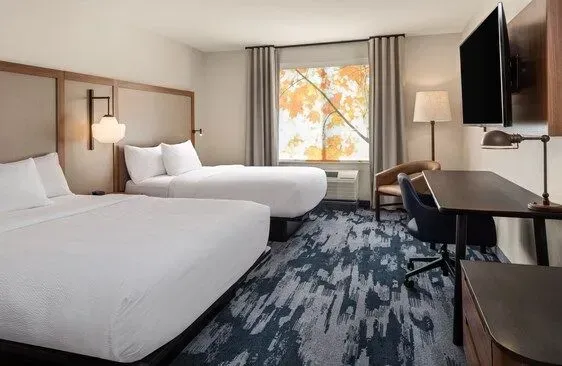 Hotel room with two white beds, desk, TV, and a window with autumn trees outside