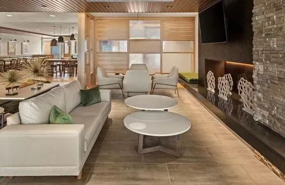 Modern lounge with white sofas, round tables, wood paneling, and a stone fireplace in a contemporary interior.