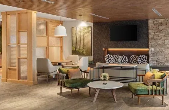 Modern lounge with green chairs, white tables, warm wood paneling, stone fireplace, and TV on the wall