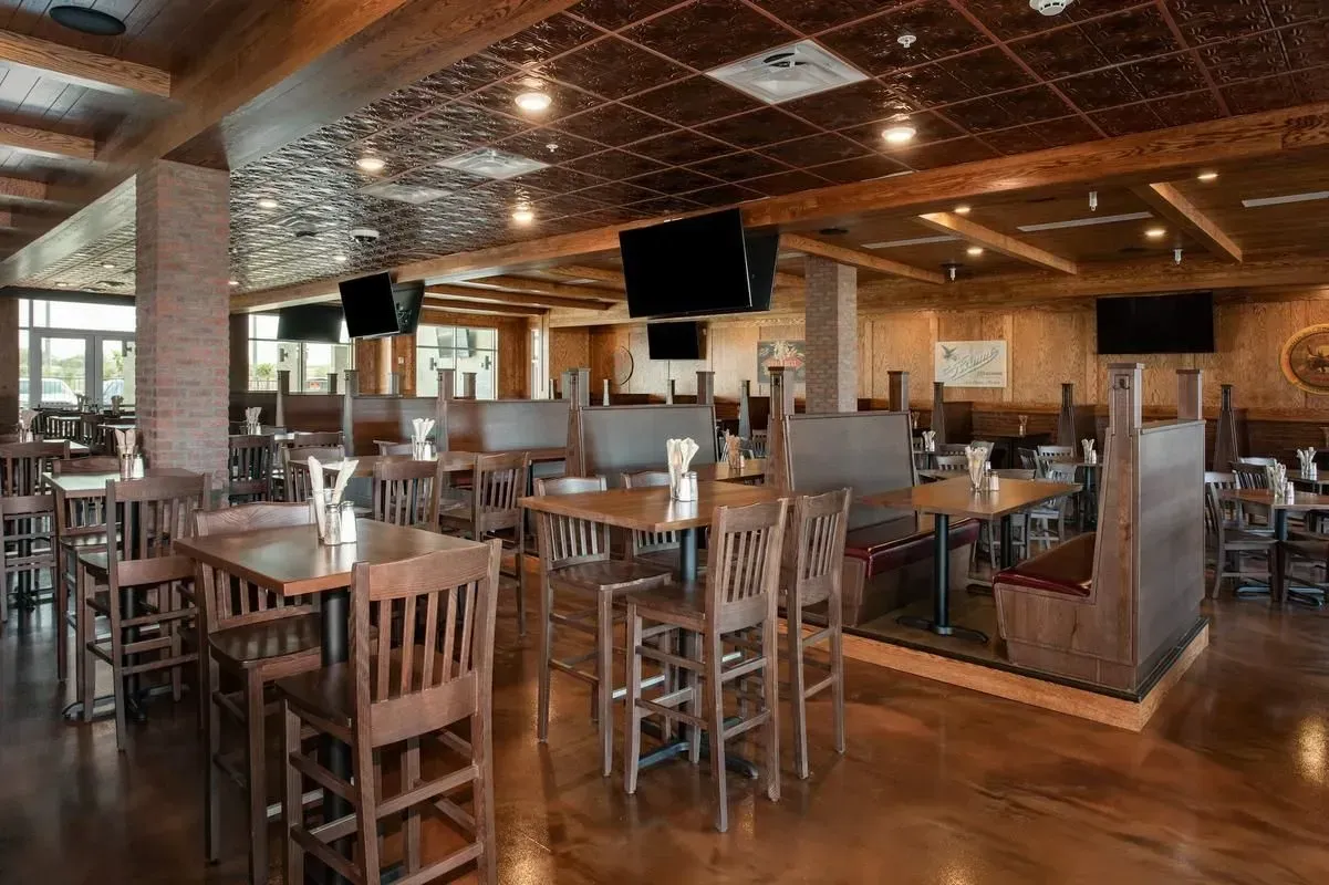 Empty restaurant dining area with wooden tables, chairs, and a polished wood floor under warm ceiling lights