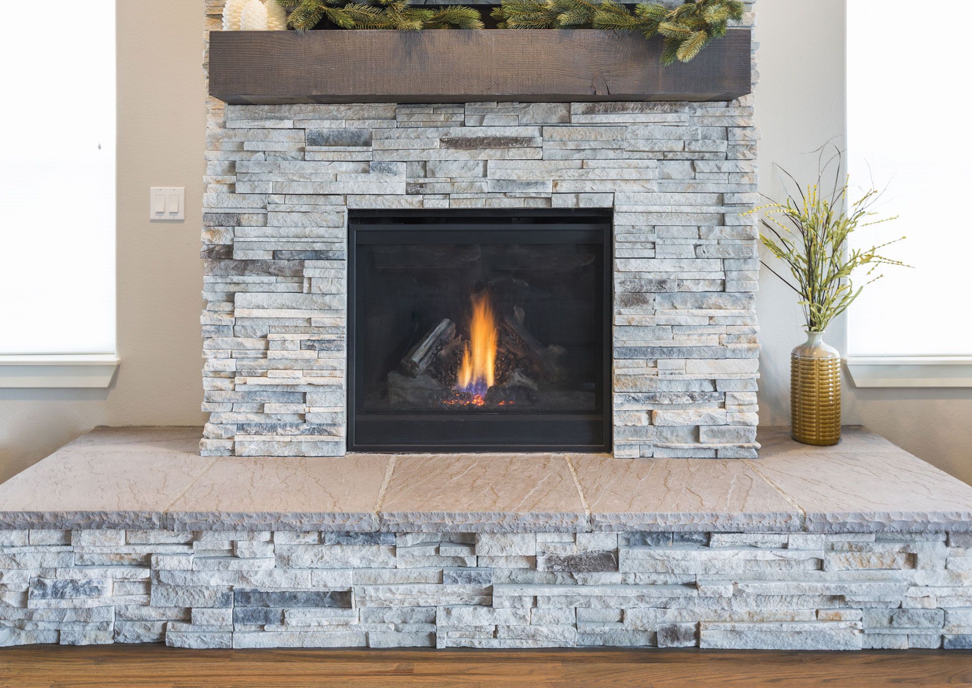 Stone fireplace with a fire, topped by a wood mantel and decorated with greenery.