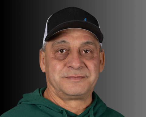 Man wearing a black and white cap and green sweatshirt, smiling. Against a gray gradient background.