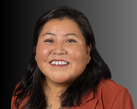 Smiling woman in a burnt orange blazer against a gradient gray background.