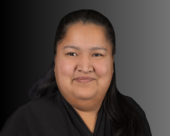 Smiling woman with dark hair, wearing a black shirt, in front of a gray gradient background.
