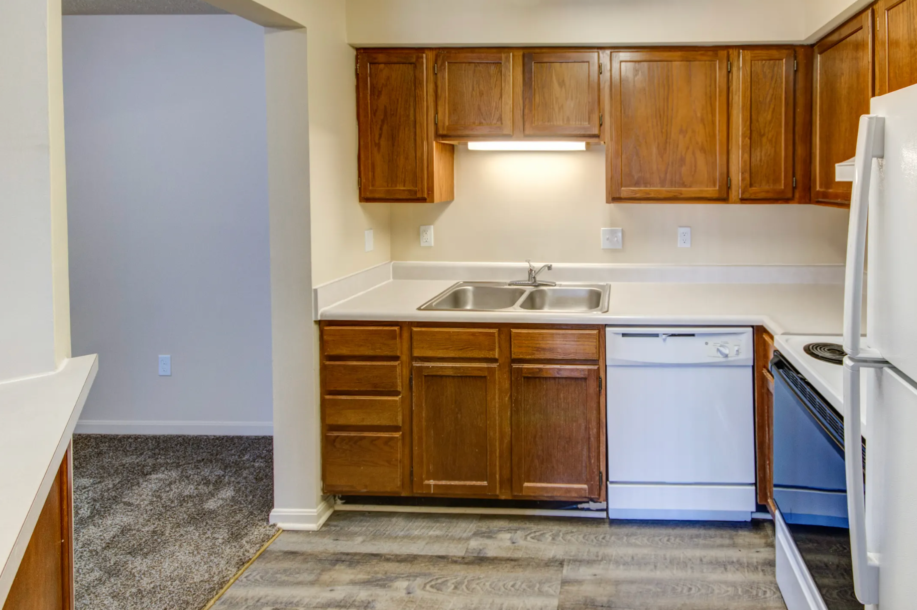 A kitchen with wooden cabinets , white appliances , a sink , and a refrigerator.