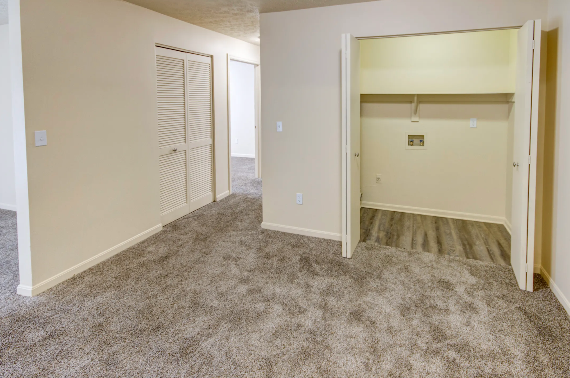An empty room with a carpeted floor and a closet.