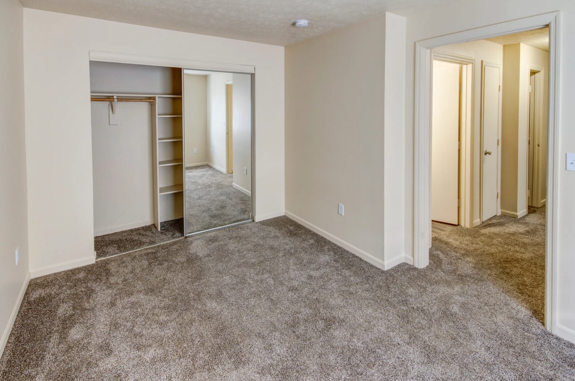 An empty bedroom with a carpeted floor and a closet.
