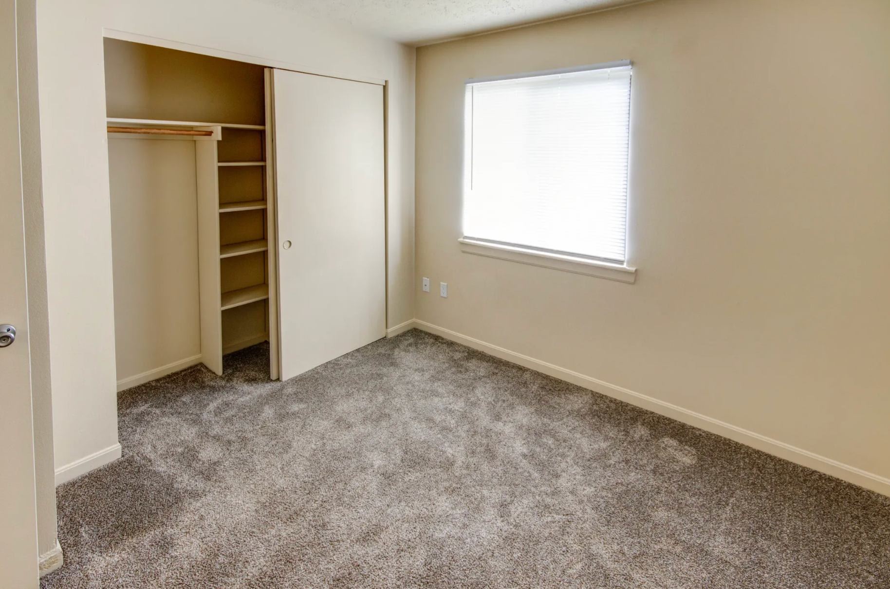 An empty bedroom with a closet and a window.