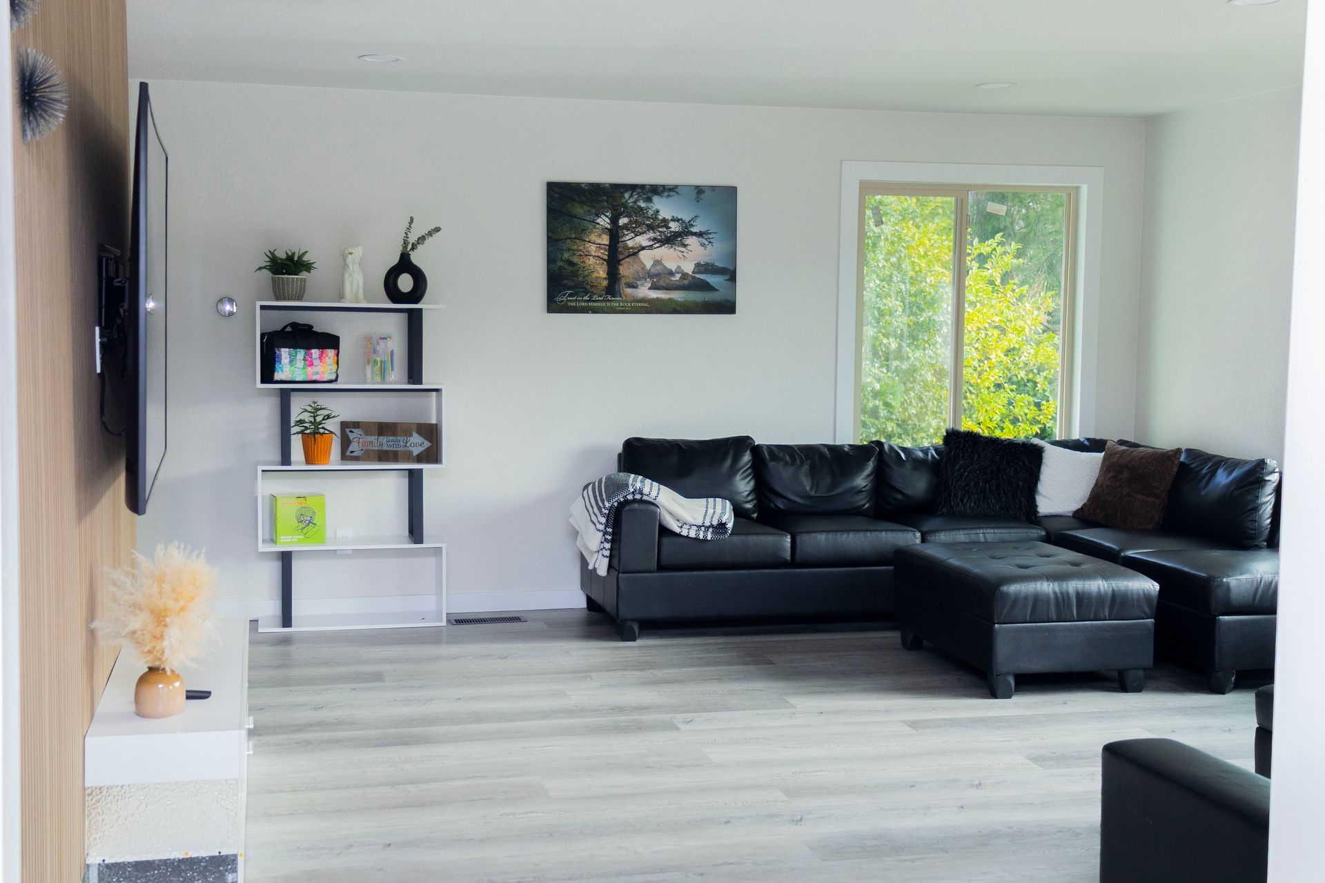 A modern living room with a black sectional sofa, a white zigzag bookshelf, and a framed landscape painting on gray walls.