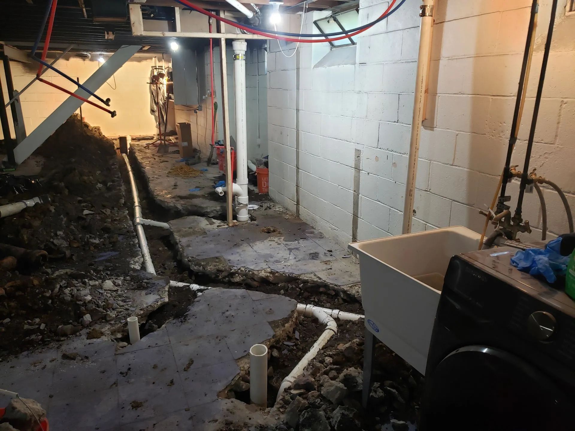 Partially finished basement with exposed pipes, concrete floor, and debris along a narrow walkway