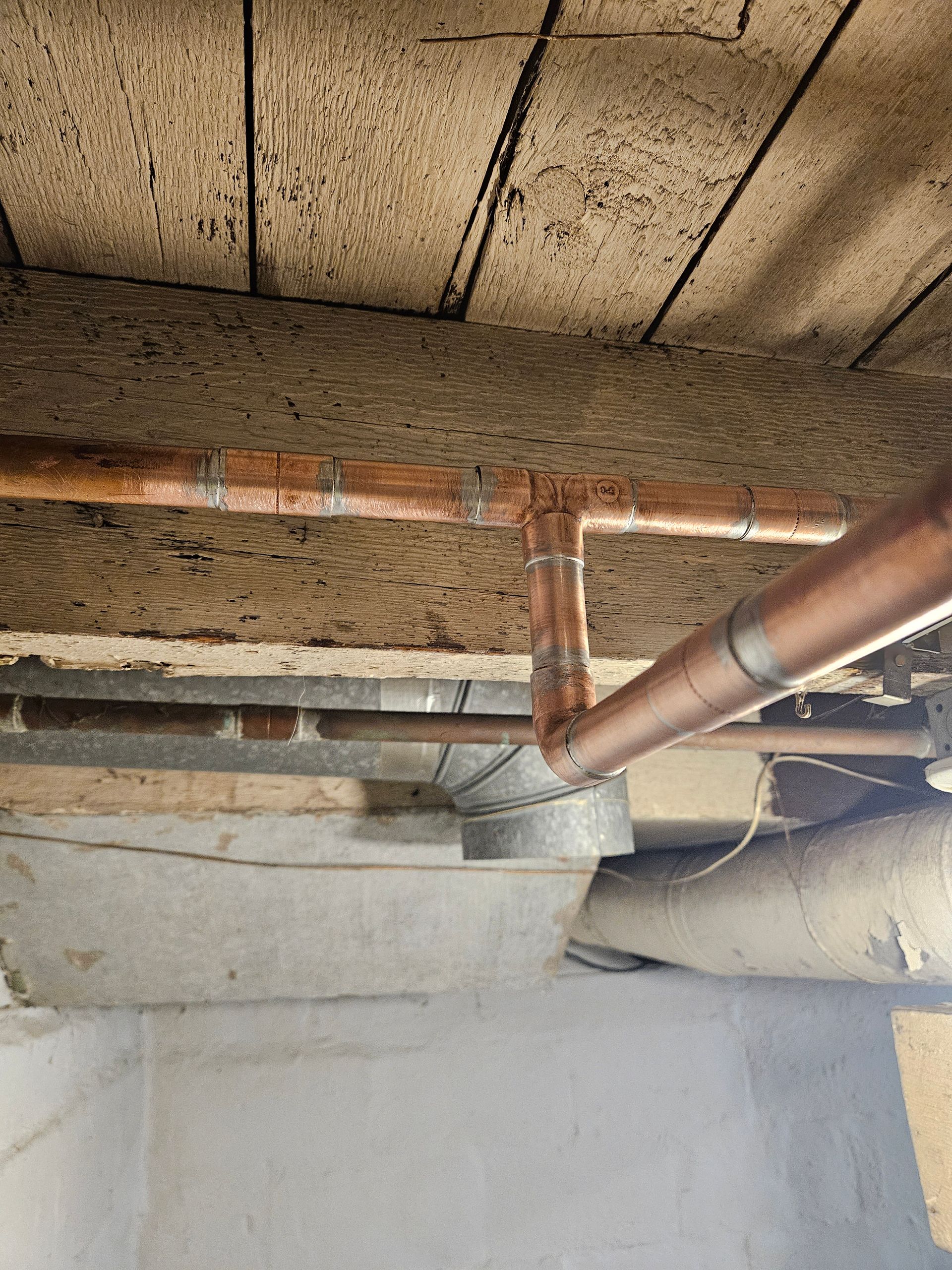 Copper pipes and a metal funnel attached to a ceiling, in a basement setting.