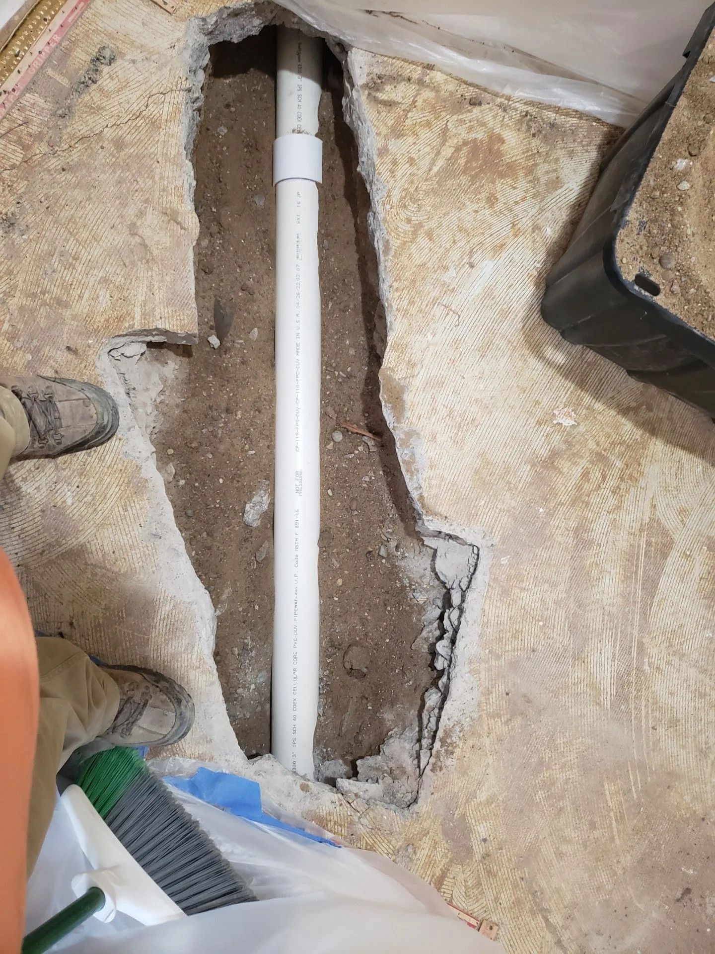 A trench cut into a concrete floor reveals a white PVC pipe laid in the dirt below.