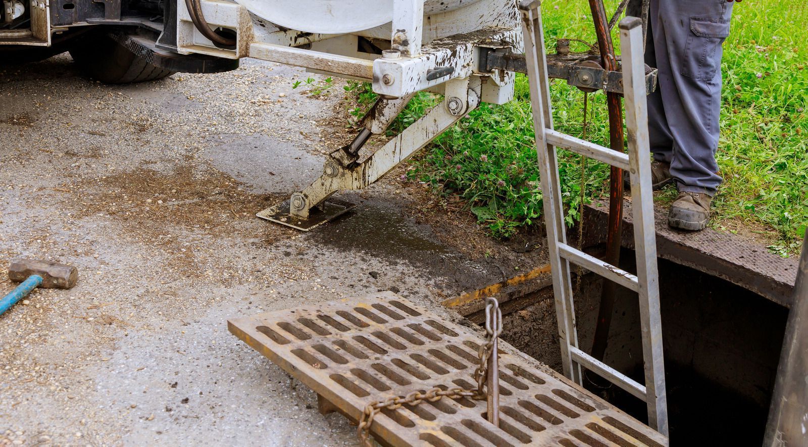Construction truck pouring concrete beside a metal drain grate and ladder in a muddy roadside ditch