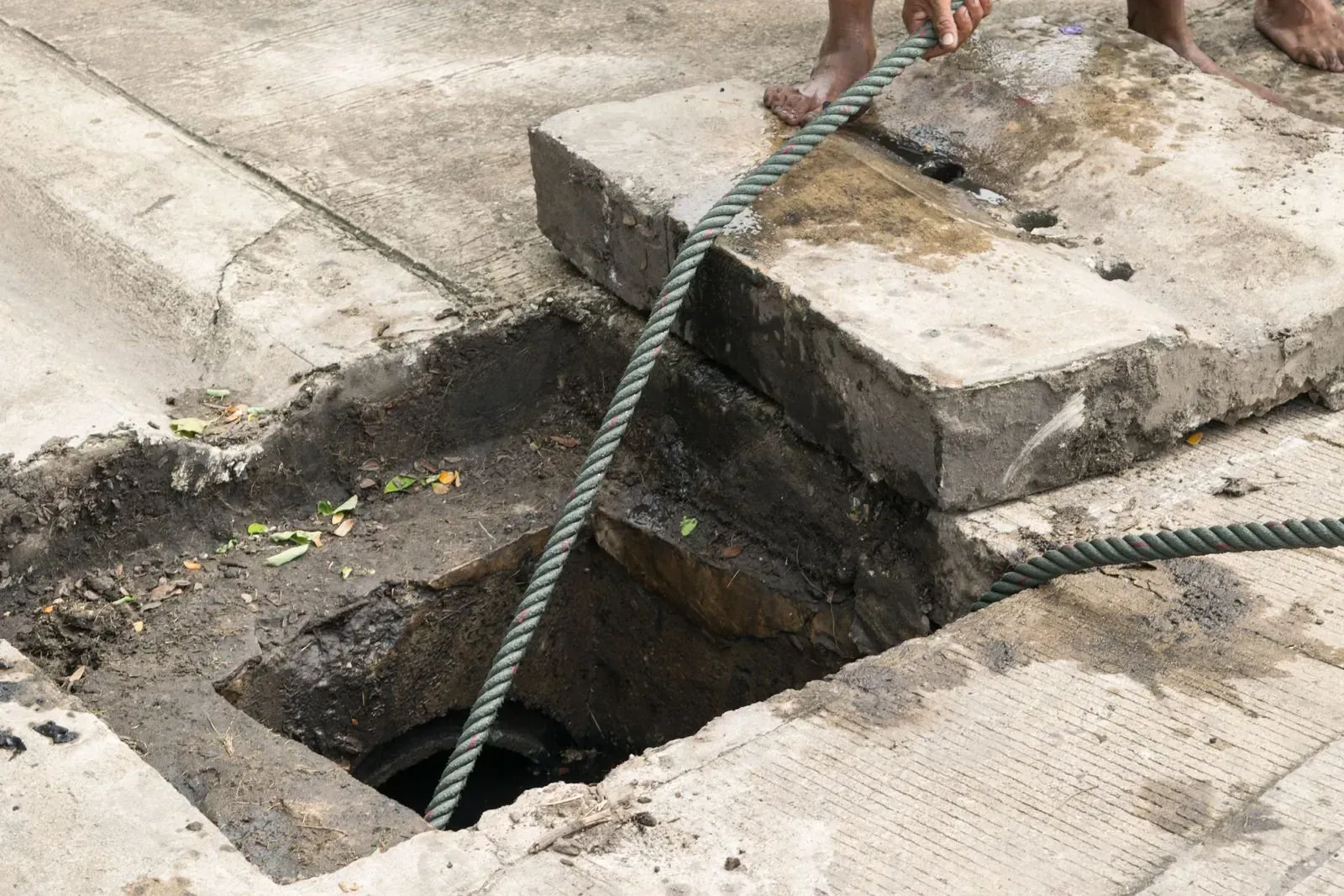 Manhole with blocks partially removed, rope lowered into the dark opening.
