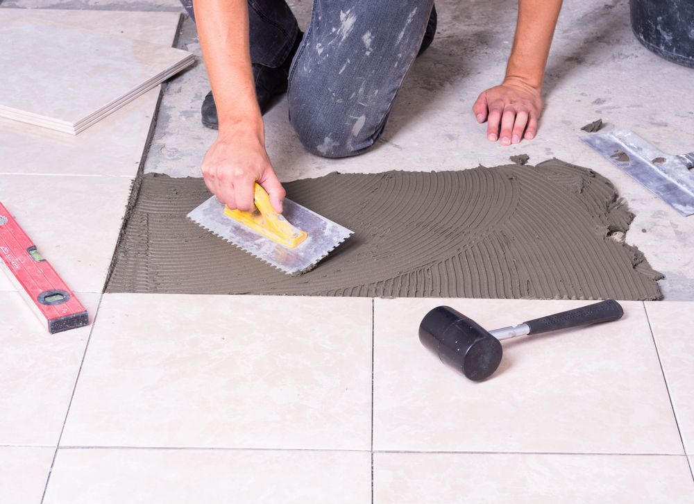 A Person Is Laying Tiles on The Floor with A Trowel — Affordable Tiling & Waterproofing in Kirwan, QLD