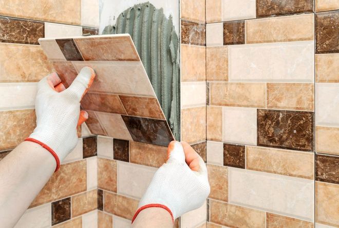 A Person Is Laying Tiles on The Wall — Affordable Tiling & Waterproofing in Kirwan, QLD