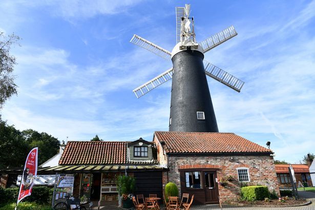 A large windmill is sitting in front of a brick building.