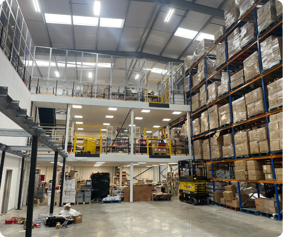Large industrial warehouse with tall pallet racks, boxes, and yellow lift equipment on a concrete floor.