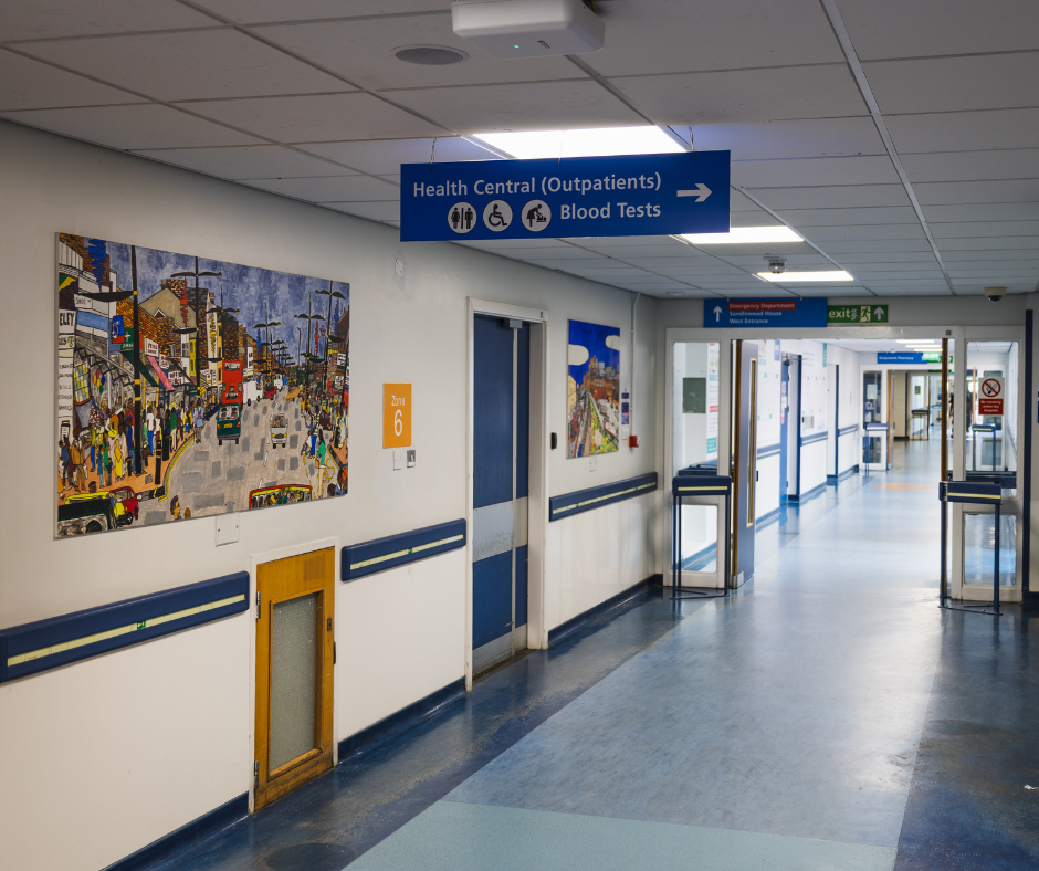 Hospital hallway with blue floor, wall art, and overhead signs pointing to health and clinic areas