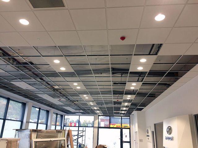 Empty office interior with a tiled ceiling, recessed lights, and large windows along one wall