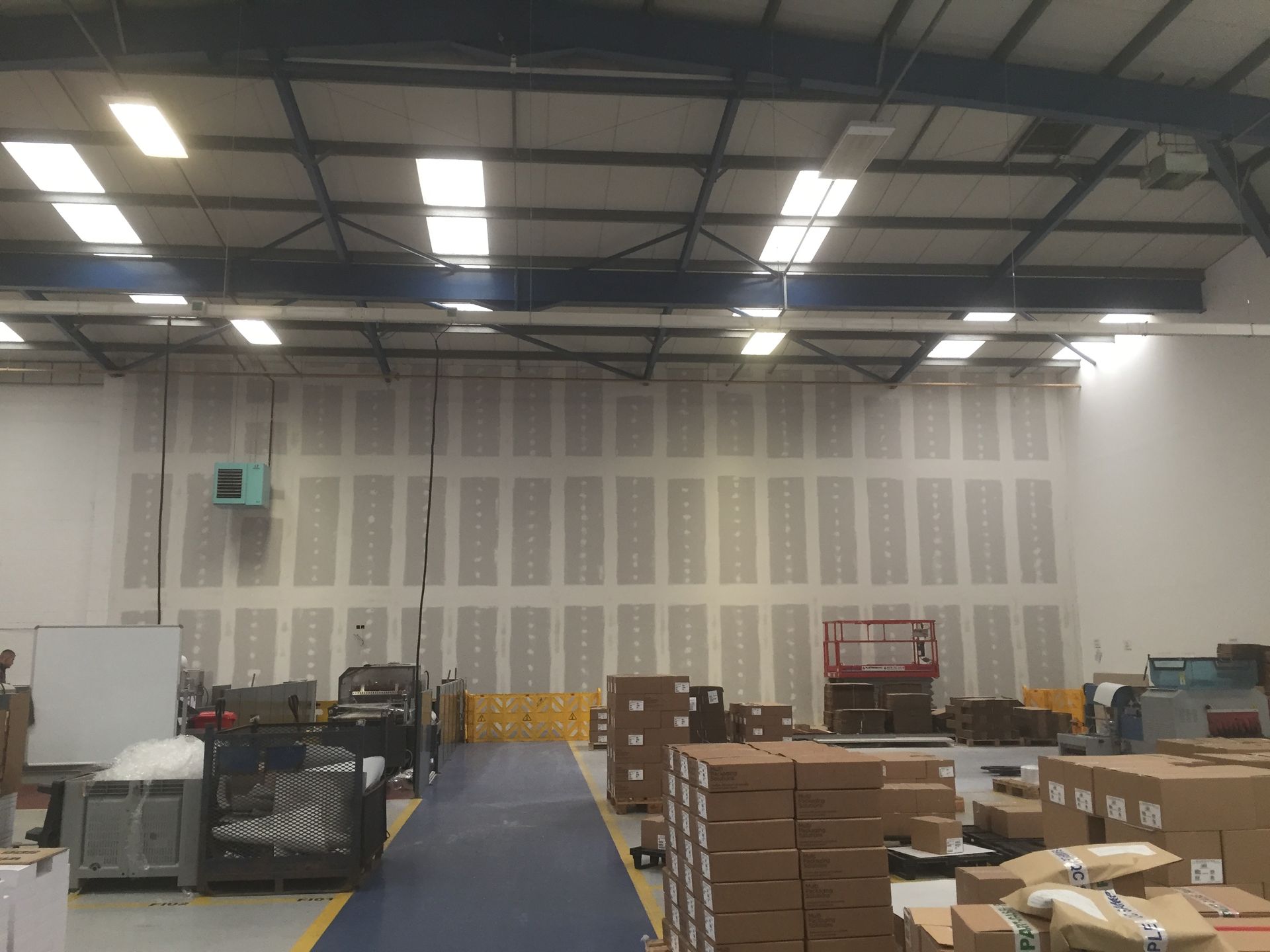 Warehouse interior with stacked boxes, shelving, and a blue aisle under bright overhead lights