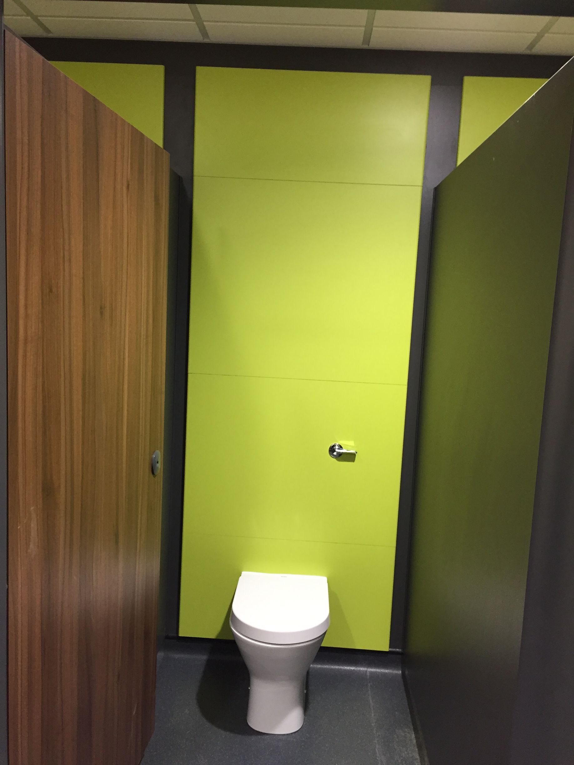 Small restroom stall with bright lime green walls, wood doors, and a white toilet.