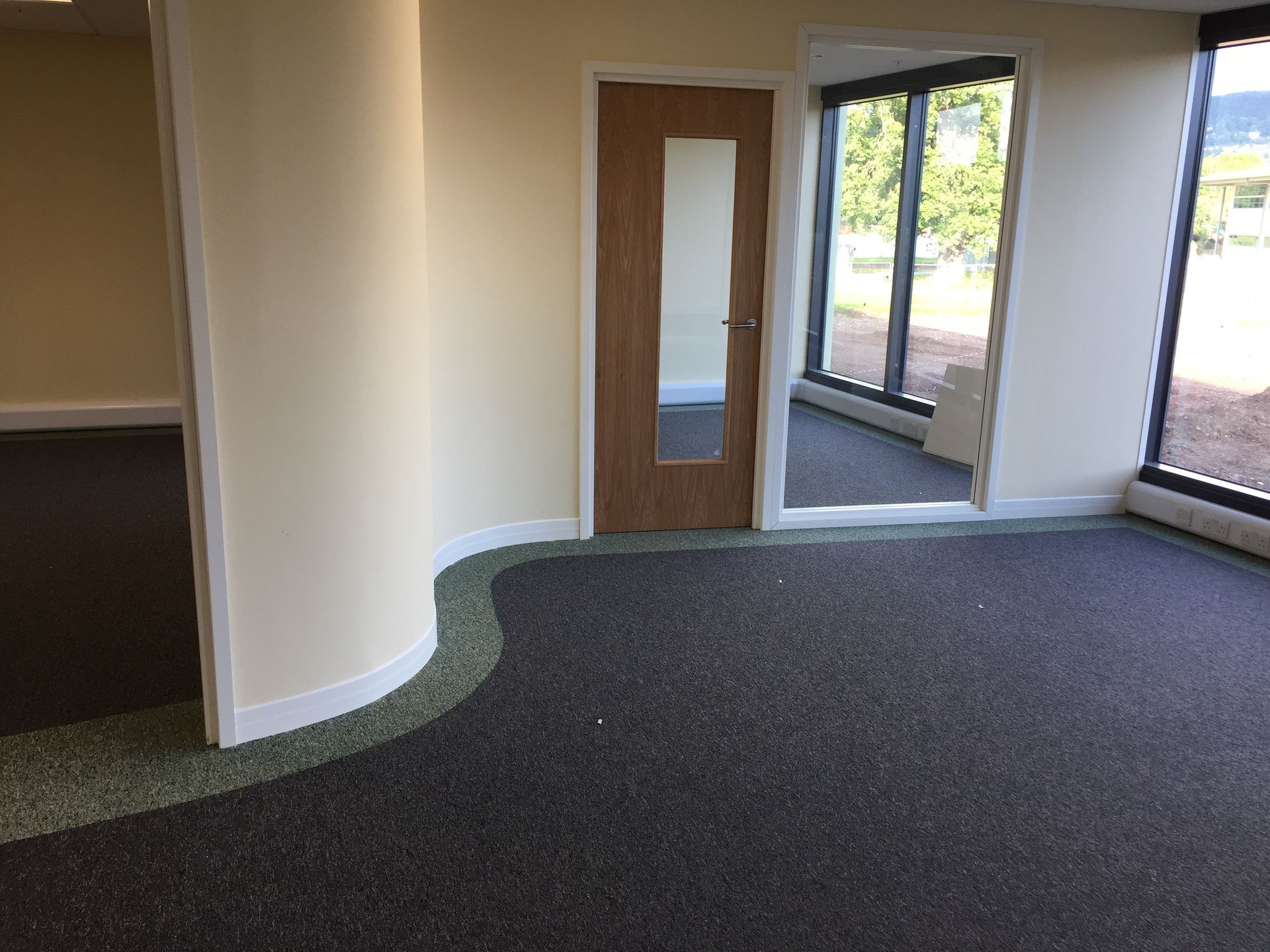 Empty office interior with carpeted floor, curved wall, and large windows and glass door.