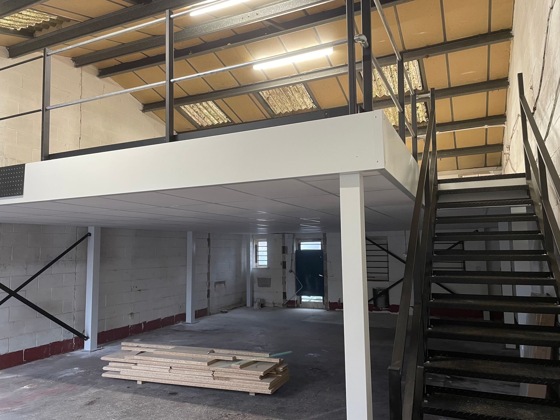 Industrial loft interior with metal staircase, mezzanine, and stacked wood planks on the floor