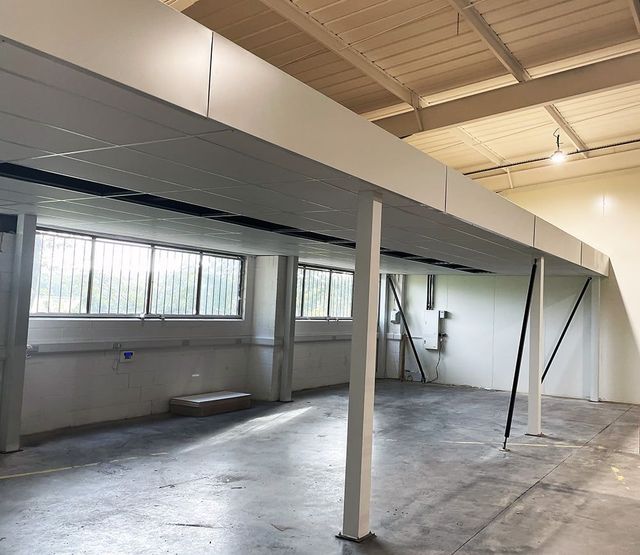 Empty industrial interior with white mezzanine, metal support posts, and high windows.