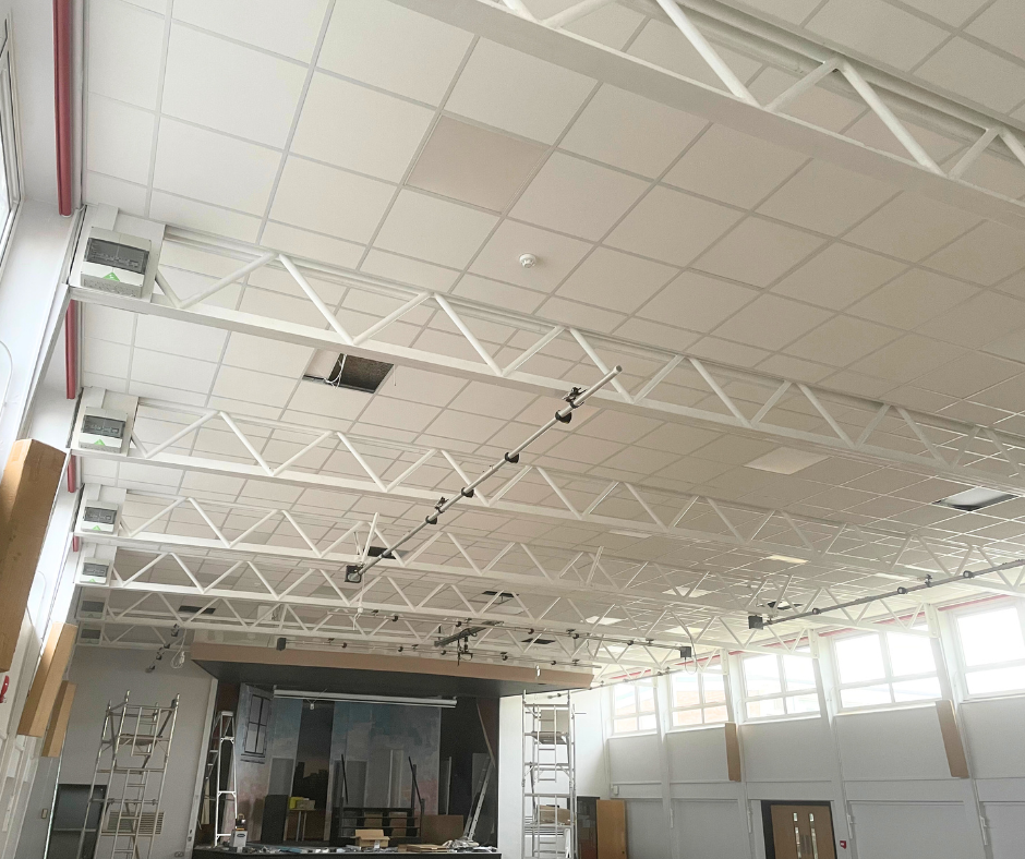 Bright empty industrial interior with white ceiling trusses, skylights, and large windows.