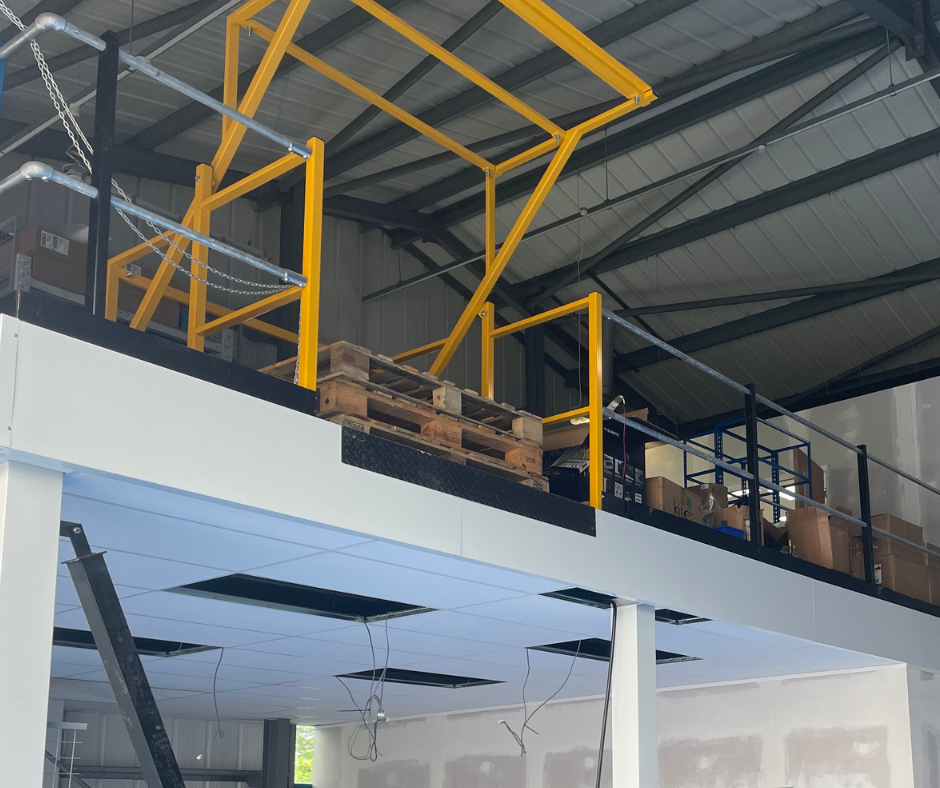 Industrial loft interior with yellow steel framing, mezzanine, stacked pallets, and high ceiling