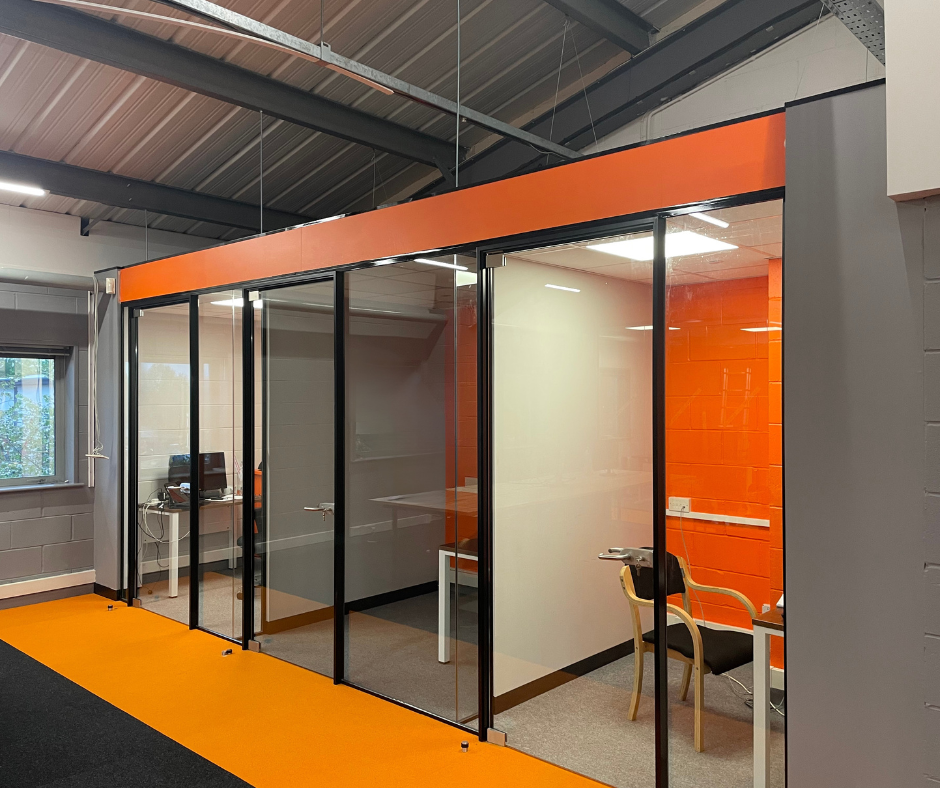 Glass office meeting room with black-framed doors and orange accent panels in a modern indoor workspace