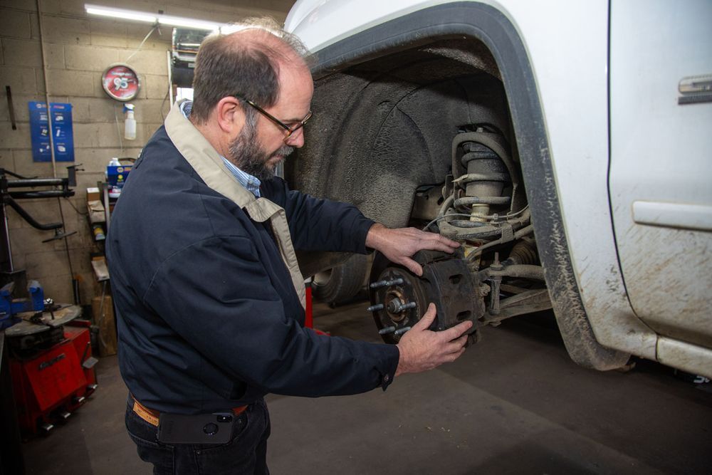 Mechanic inspecting a truck’s exposed front wheel assembly | Scott's Ivy Exxon Automotive & Tire