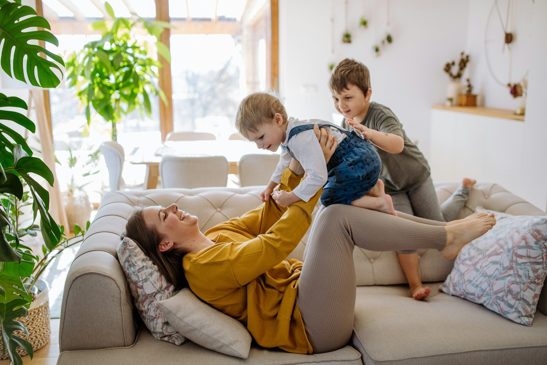 Woman lying on a sofa playing with two children in a bright living room