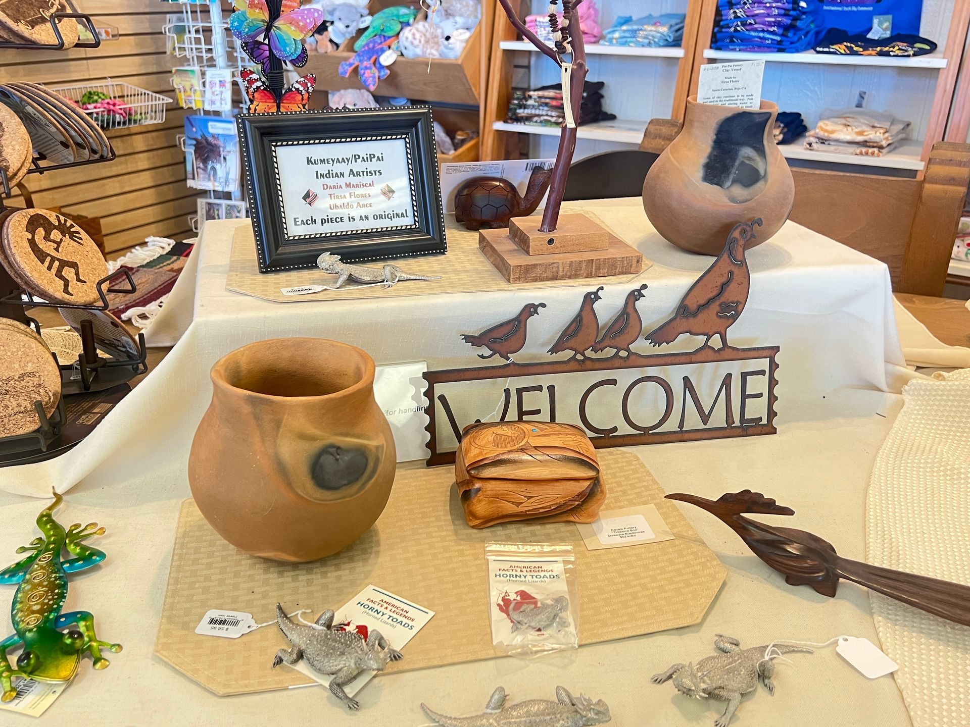 Rustic welcome display with pottery, bird figurines, jewelry, and a framed sign on a table.