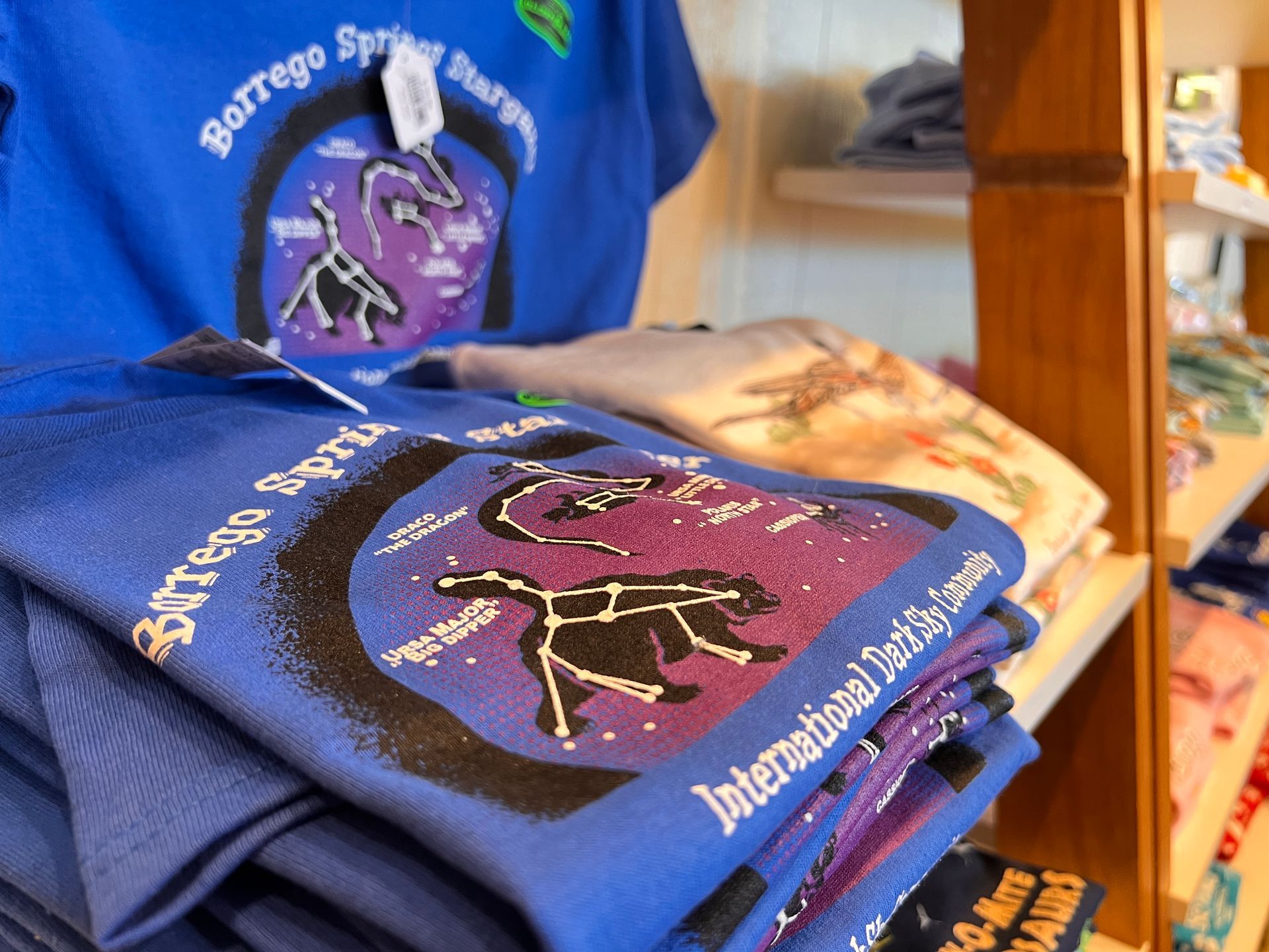 Stacked blue shirts with a purple deer graphic and white text on a store shelf.