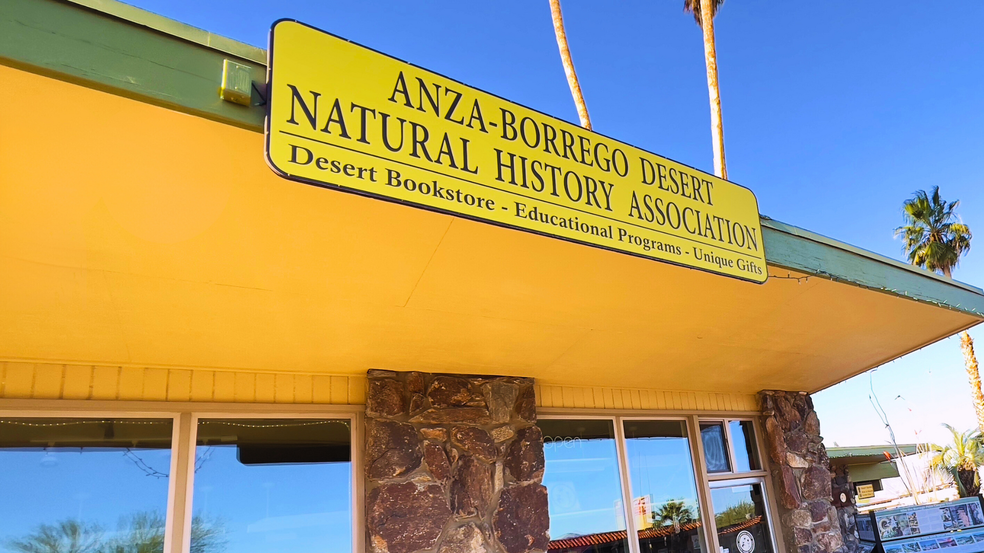 Visit Website Yellow sign for Anza-Borrego Desert Natural History Association on a building entrance under a clear blue sky