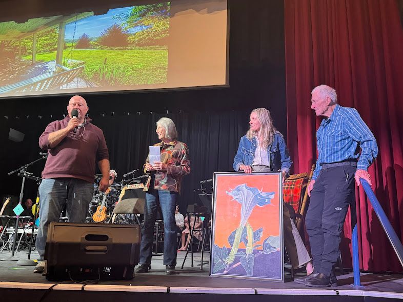 Four people on a stage at a speaking event, with a projected landscape behind them and a red curtain backdrop
