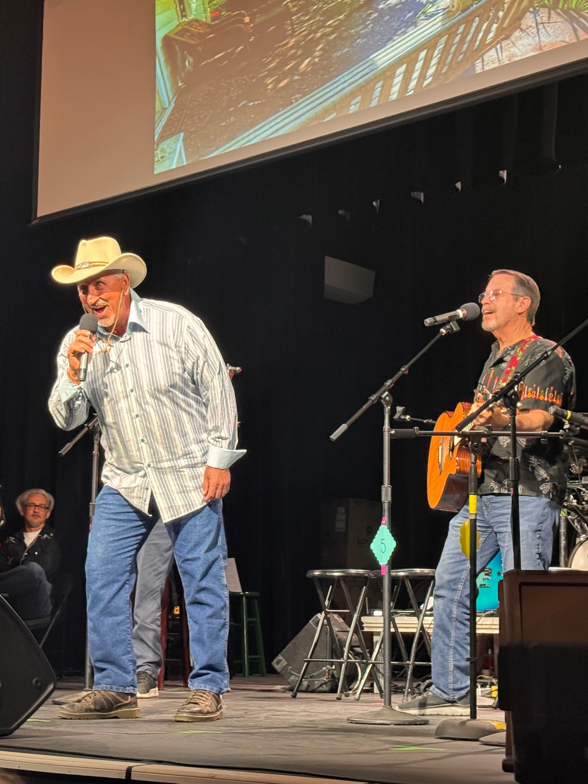 Two musicians onstage, one in a cowboy hat singing into a microphone and one playing guitar