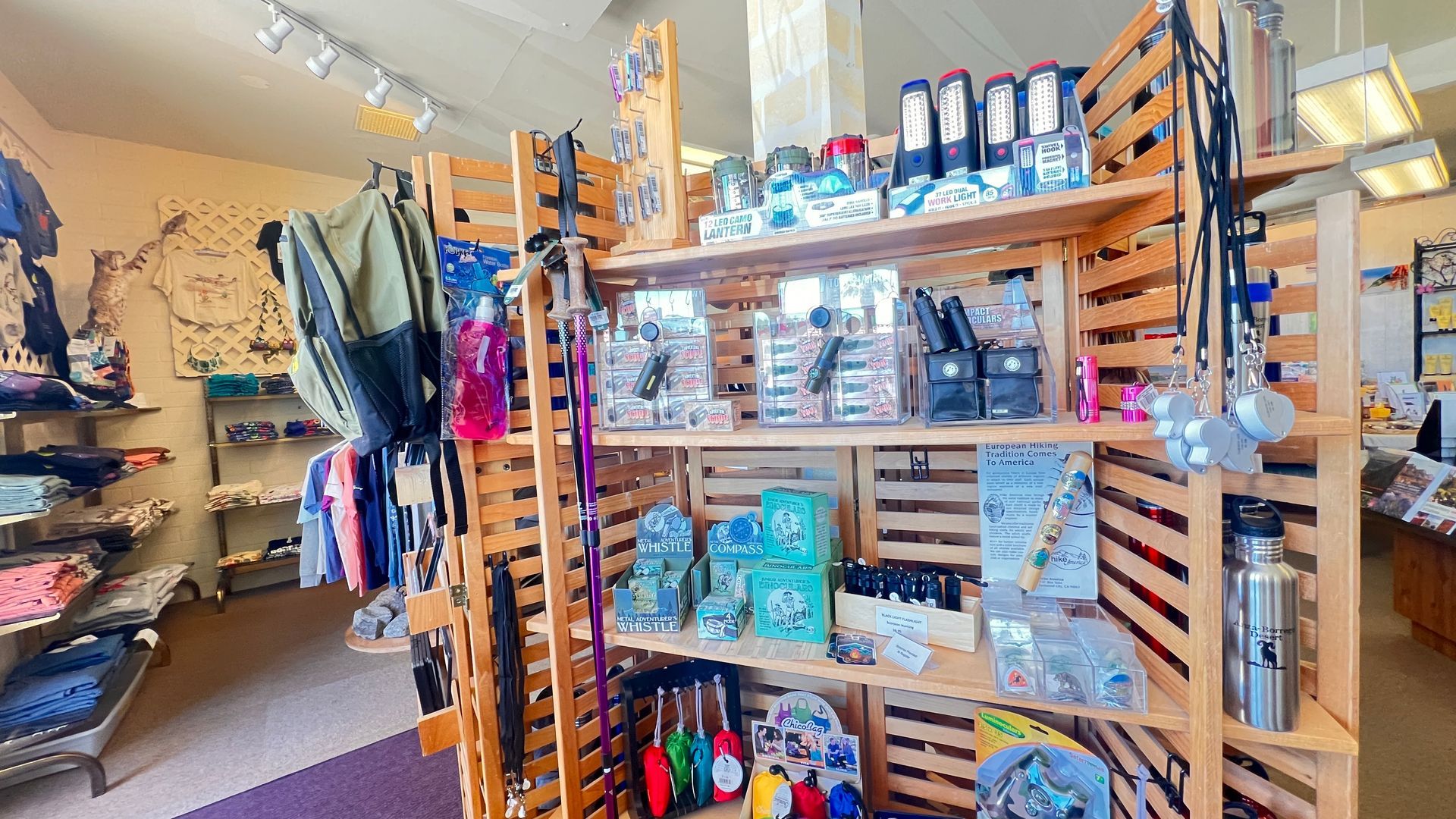 Retail store shelves stocked with colorful packaged goods, clothing racks, and wooden display tables