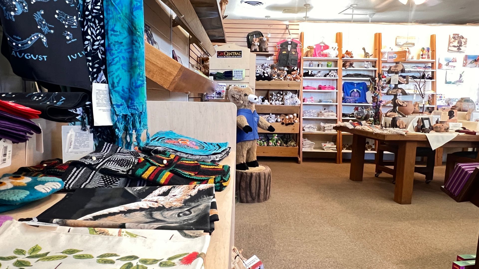 Brightly lit boutique with colorful folded textiles, wooden tables, and shelves of crafts and gifts