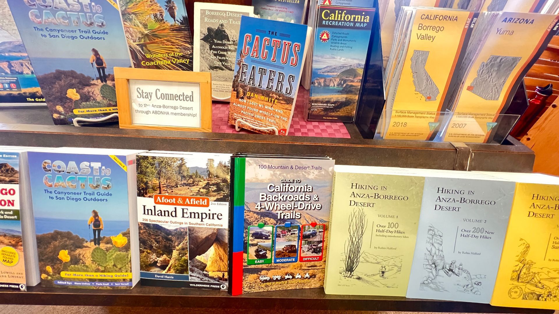 Travel brochures and maps displayed on a wooden rack, with colorful postcards and handwritten notes below.