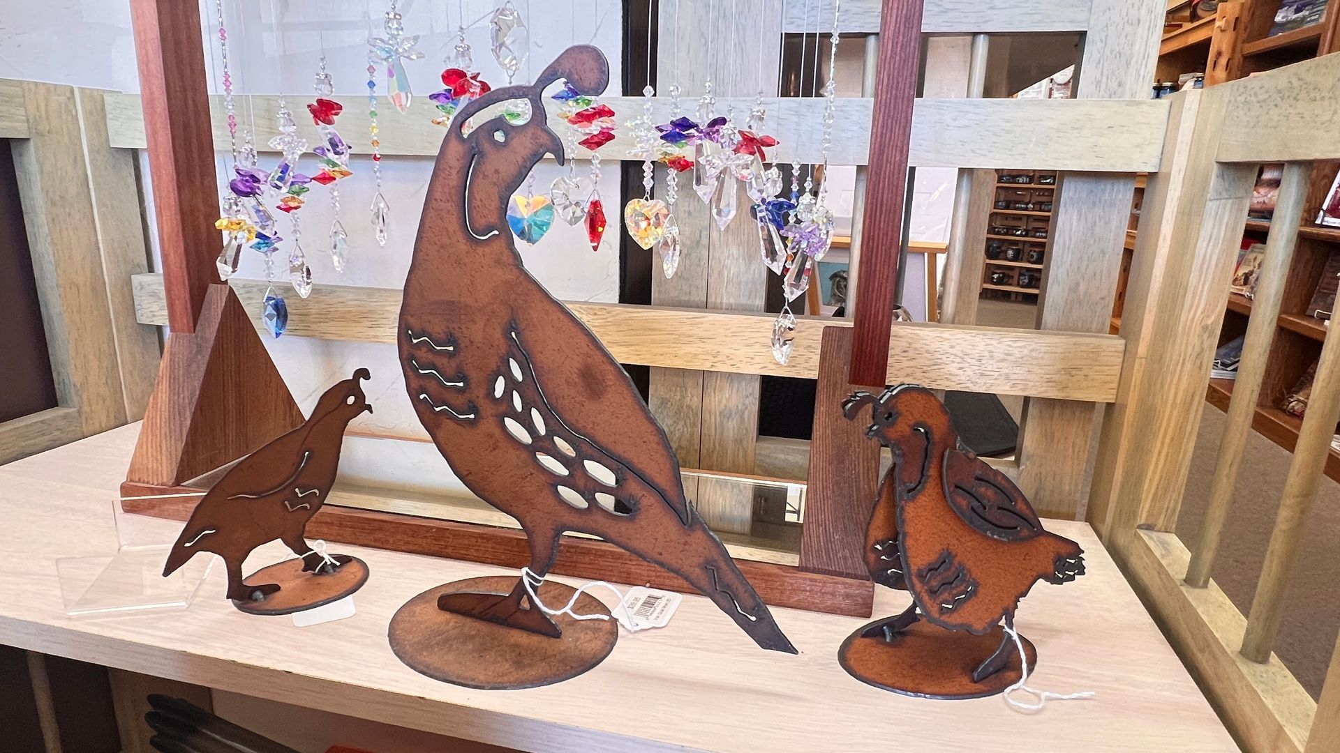 Rust-colored metal bird sculptures displayed indoors on a wooden shelf, with a larger bird in the center
