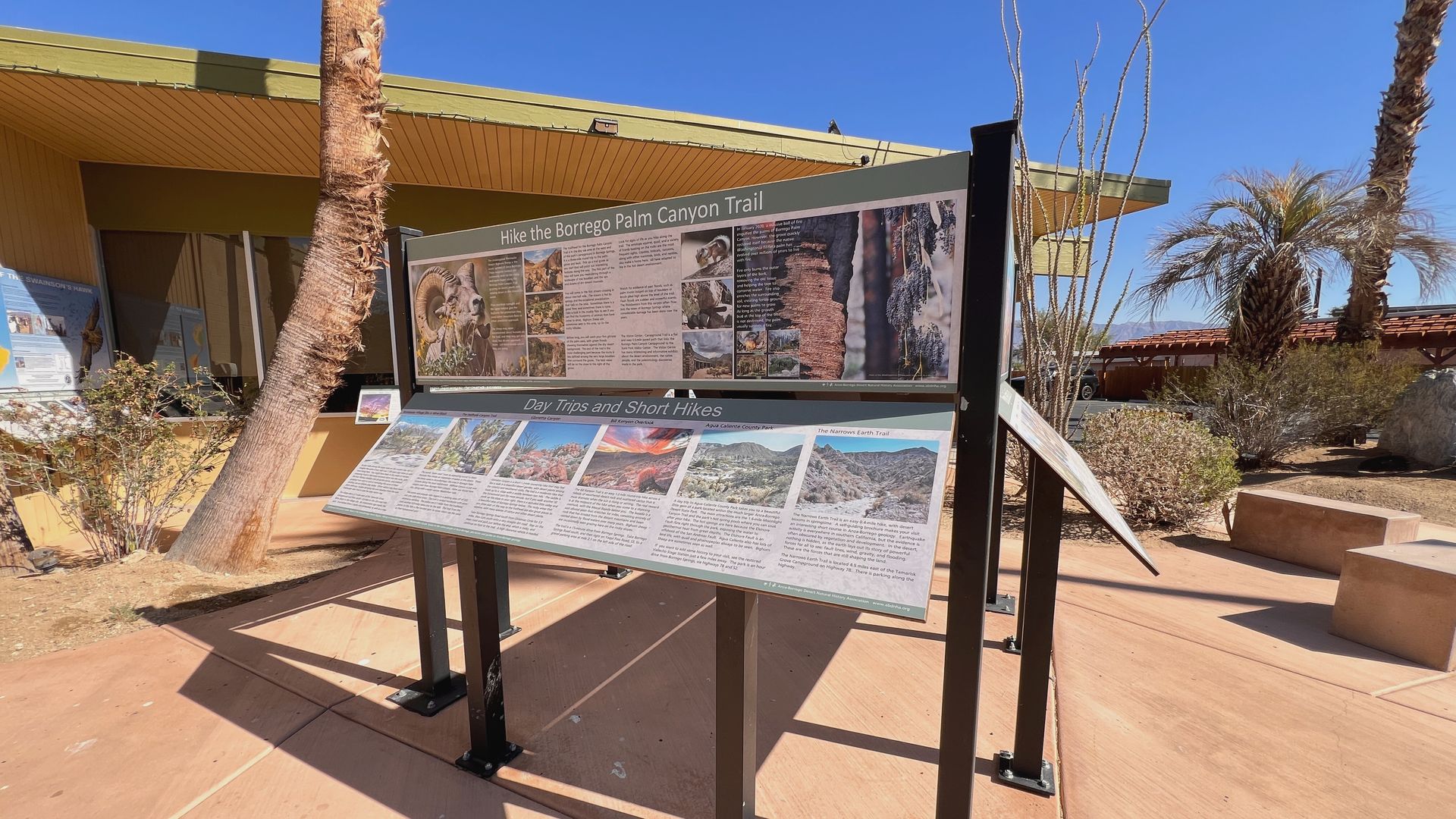 Outdoor information sign with maps and text panels in a sunny desert courtyard