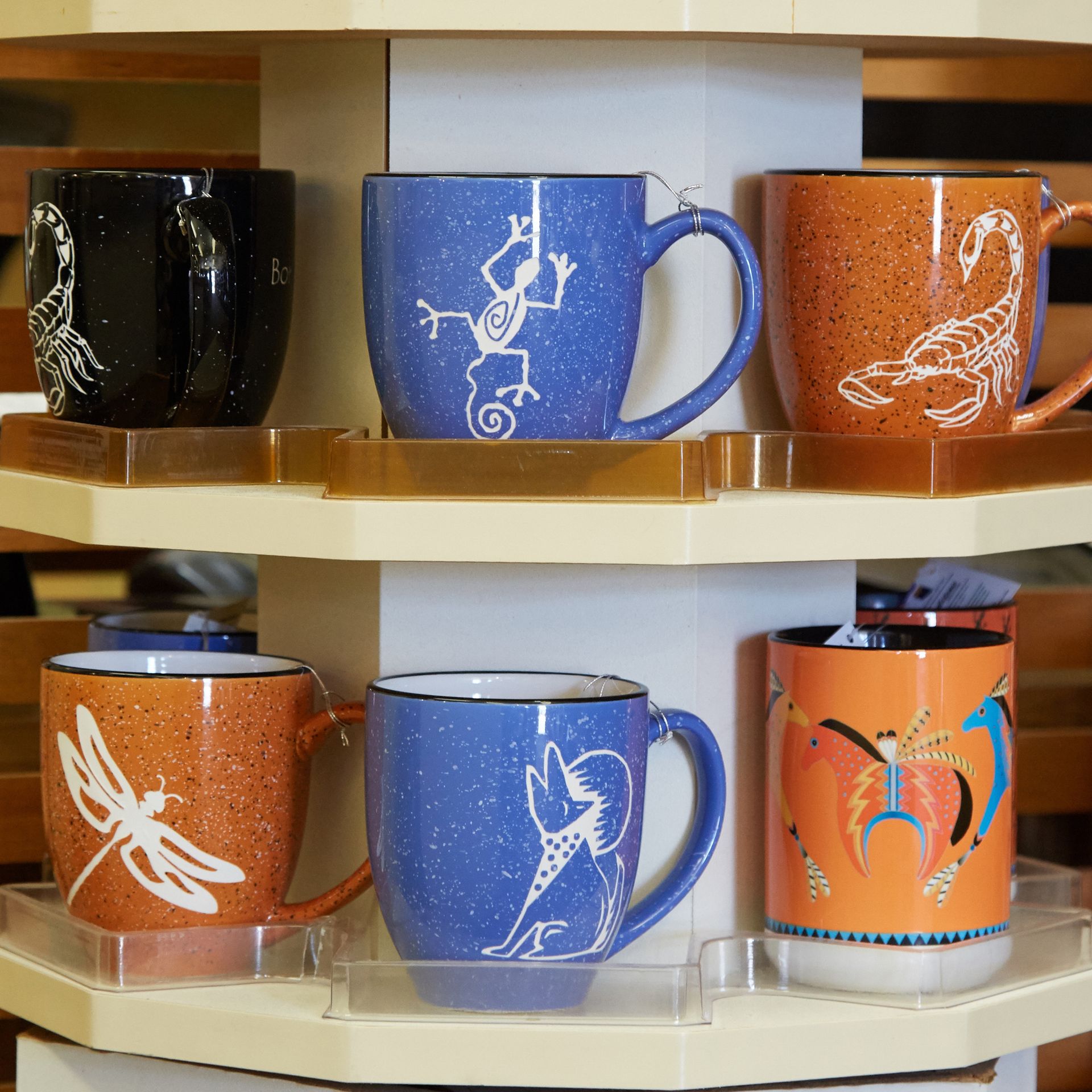 Six colorful ceramic mugs on a shelf, each with white bird designs.