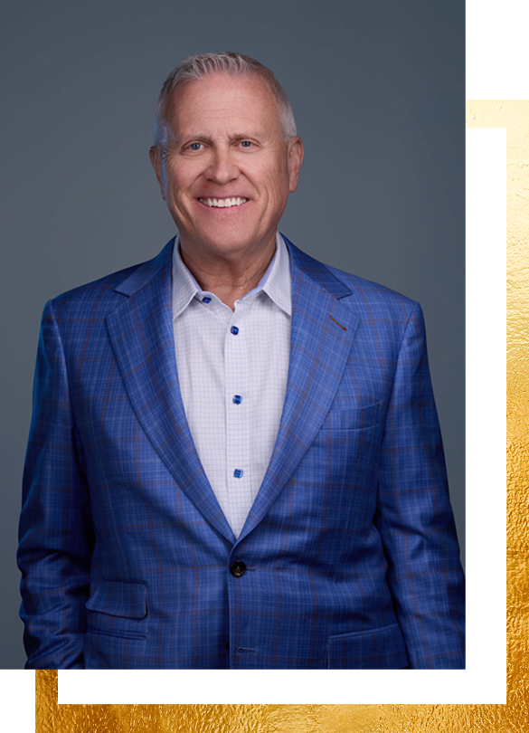 Man in blue plaid suit smiling, standing in front of a gray background.