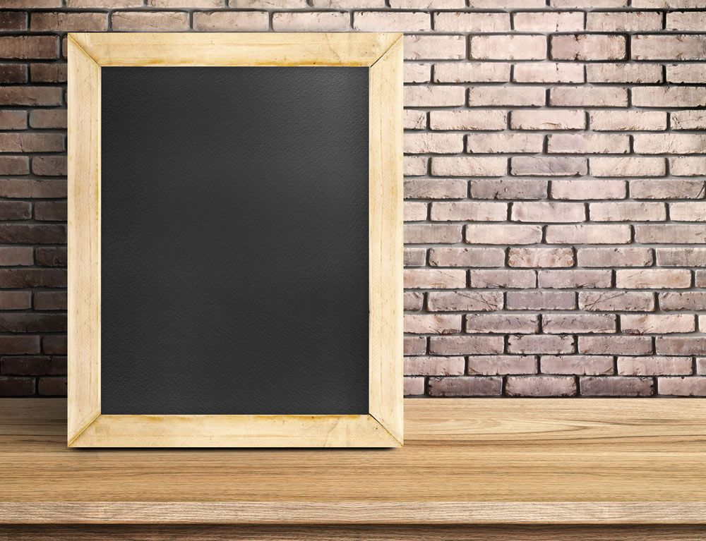 A Blackboard Is Sitting on A Wooden Table in Front of A Brick Wall — The Framer In Taree, NSW